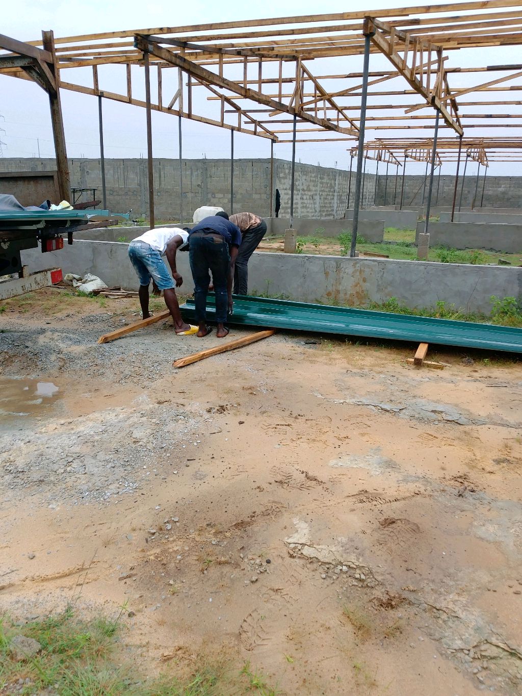 Trois ouvriers préparant des tôles métalliques vertes sous une charpente métallique en construction